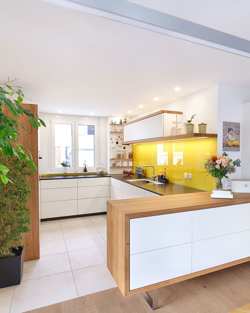 Maßgefertigte Küche aus Holz und weißen Fronten mit gelber Glasrückwand und Kücheninsel vom Schreiner gefertigt
