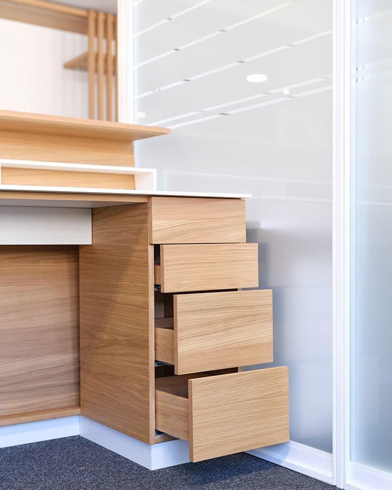 Detailansicht eines maßgefertigten Büromöbels mit Holz-Auszügen und integrierter Arbeitsfläche von der Echaz Schreinerei